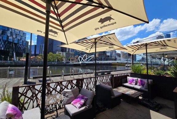 Cafe tables, seating and umbrellas overlooking the Yarra River.