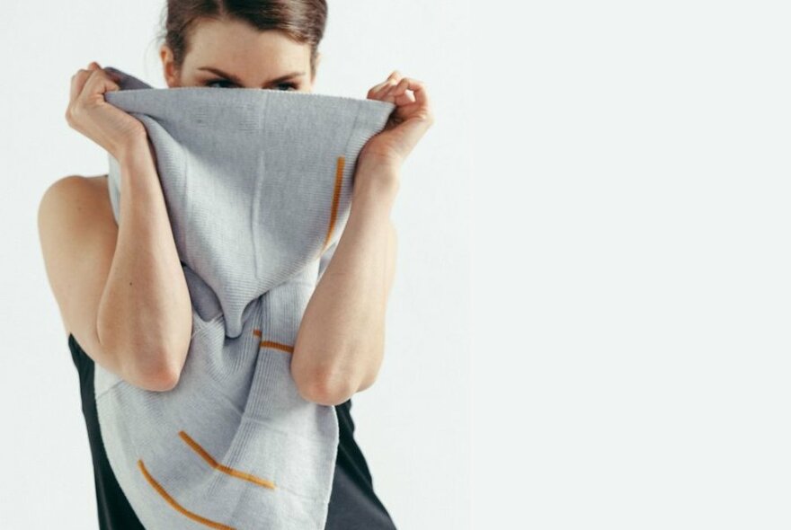 A model posing with a grey and yellow infinity scarf pulled over her face.