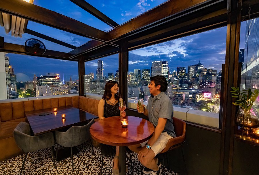 A couple drinking on a rooftop bar at sunset.