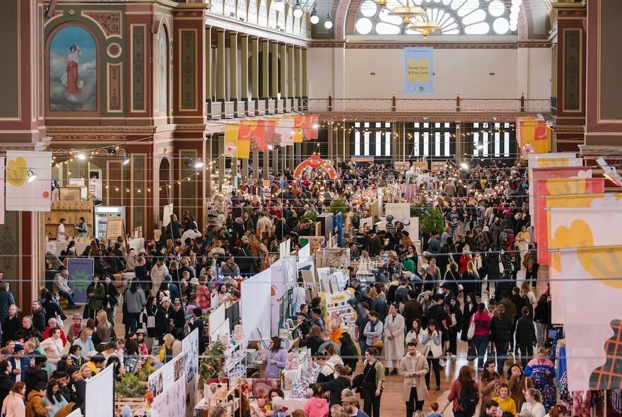 Large crowds of people wandering around stalls at the indoor design market inside the Royal Exhibition Buildings.