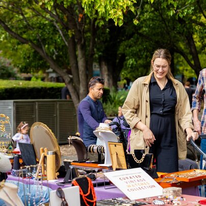 People browsing an outdoor market bric-a-brac stall in a park location.