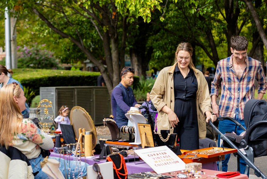 People browsing an outdoor market bric-a-brac stall in a park location.