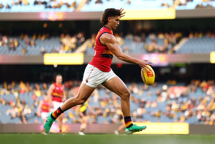 An Adelaide Crows AFL football player running and about to kick the footy, on the field during a match.