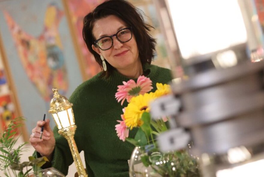 Tutor and teacher artist Debra Longin smiling and standing behind a vase of flowers.