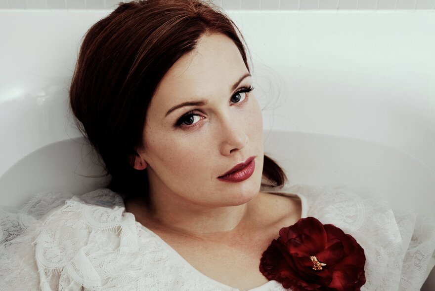 Singer Clare Bowditch, floating in a white bath with a red flower.