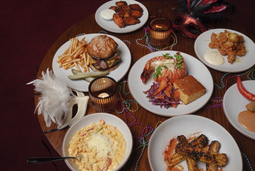 A selection of Southern American dishes presented on a round wooden table with candles and a white burlesque mask.