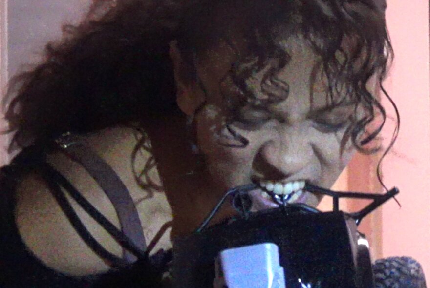 A woman with ringlets of hair on her forehead lifting an object with her teeth.