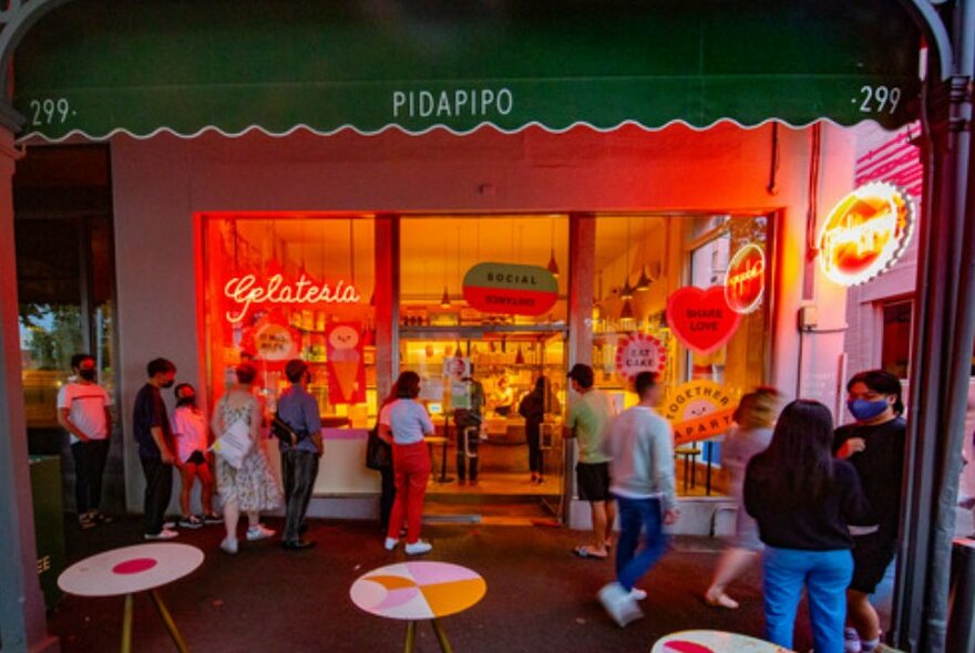 People lining up outside an ice cream shop with neon lighting.