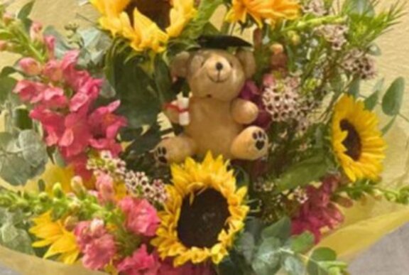 Bouquet of flowers with sunflowers and teddy wearing a mortar board.