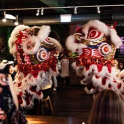 Two red and white Lion Dance lions meeting face to face in a restaurant setting.
