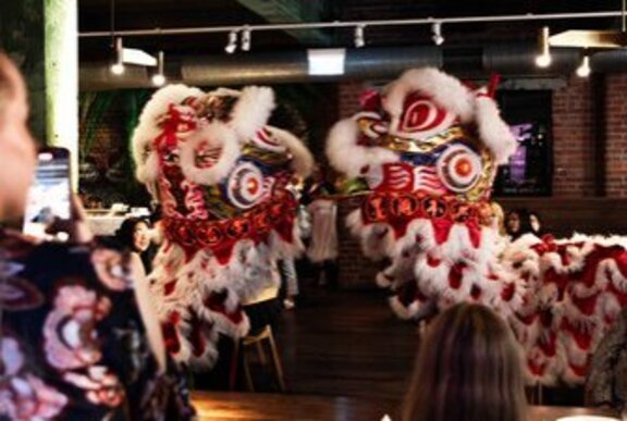 Two red and white Lion Dance lions meeting face to face in a restaurant setting.