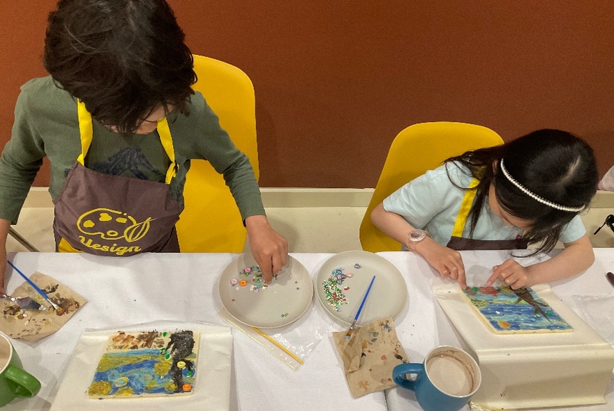 Two kids with heads down working on painting projects. 