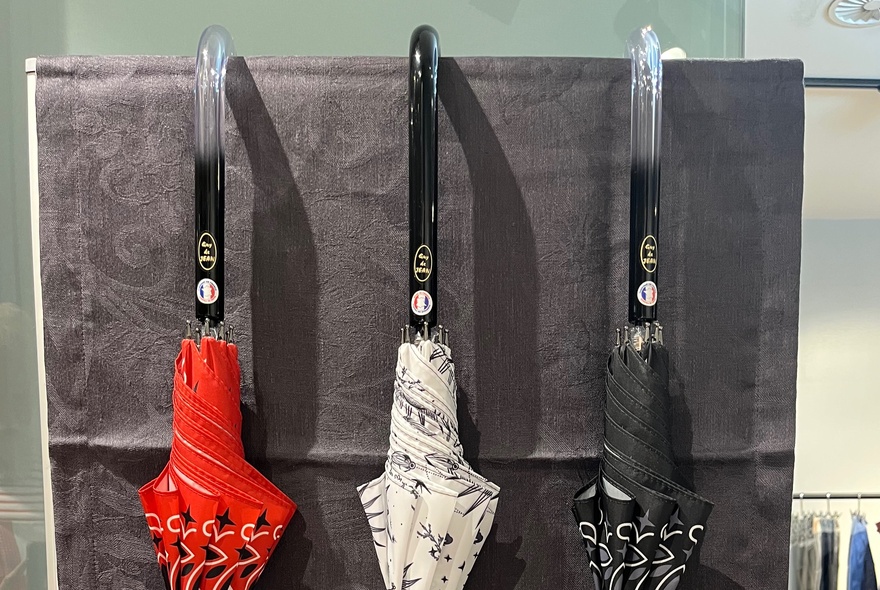 Three different coloured umbrellas (down) hooked over piece of grey cloth. 