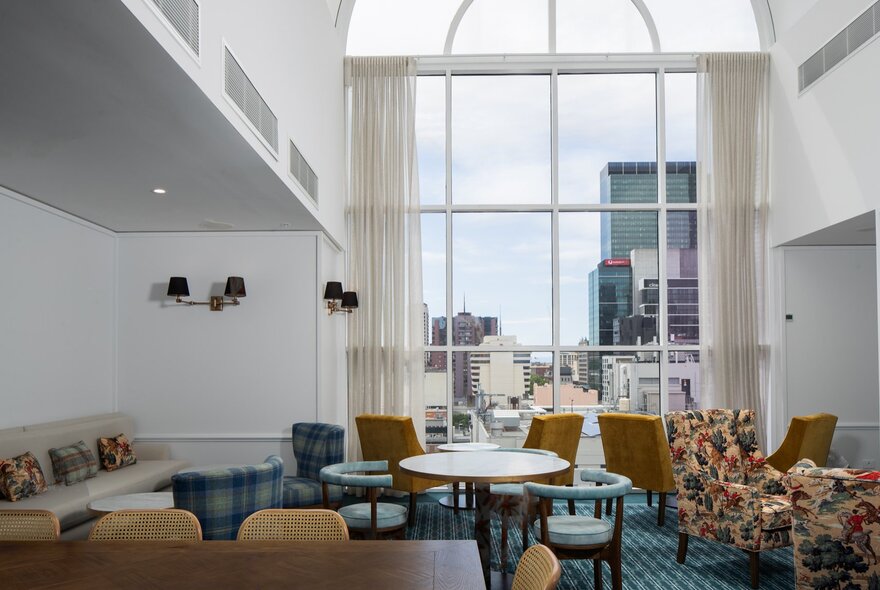 The Elevate Club Lounge at Pullman Melbourne City Centre, with armchairs arranged around low tables and a large arched rear window with views of city buildings.