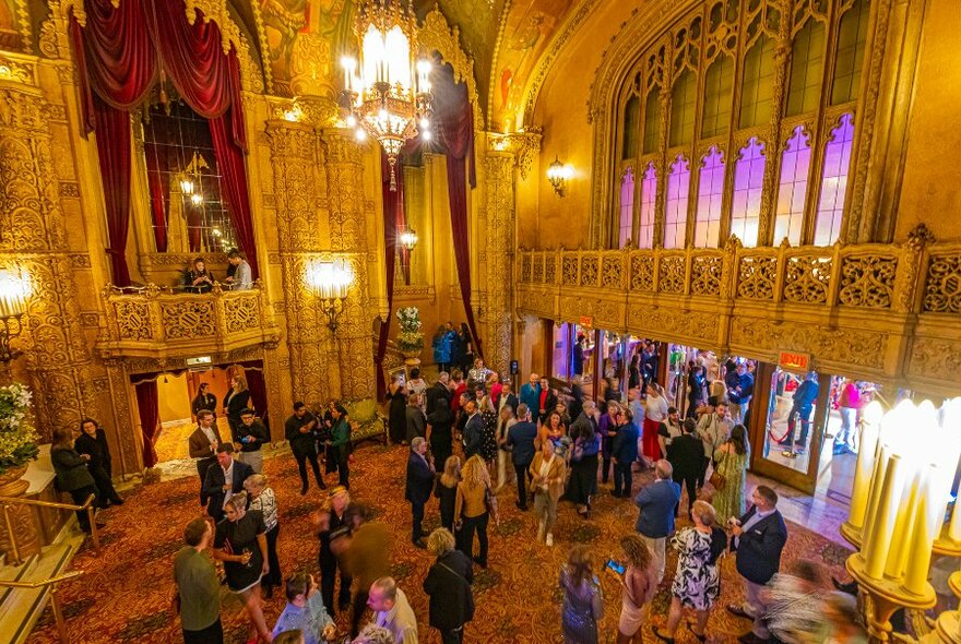 An ornate theatre interior with people milling around before a show.