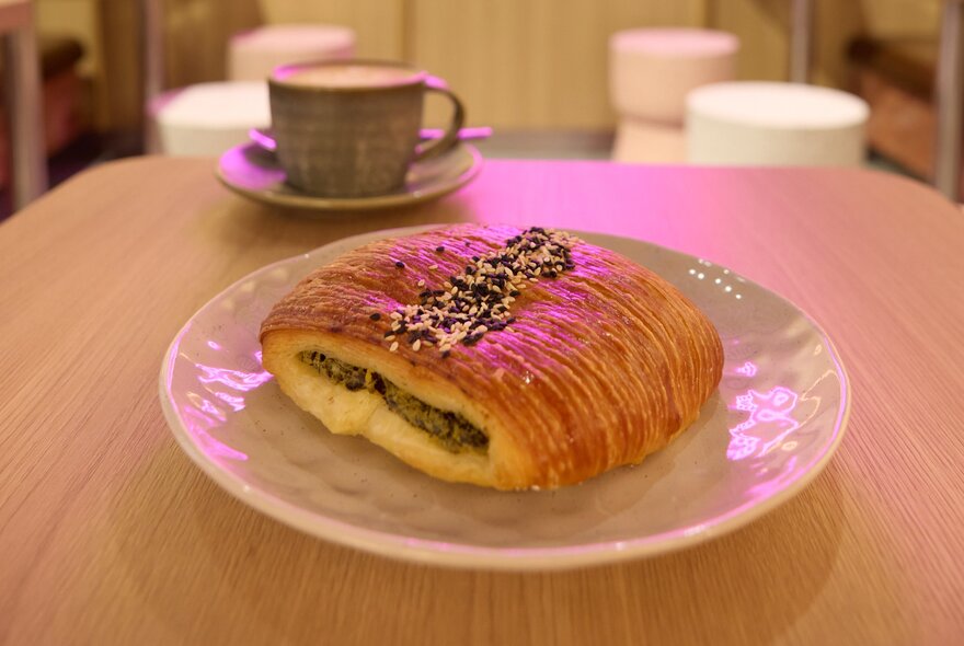 A silverbeet, kale and feta croissant on a plate and a coffee mug in the background.