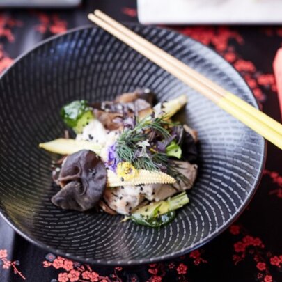 A dish of food served in a shallow black bowl, with chopsticks resting on the side of the bowl.