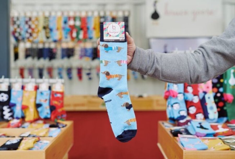 A person in a shop holding a pair of socks with a sausage dog print.