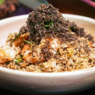 An earthenware dish with prawn fried rice, featuring a pile of grated black truffle on top as garnish.