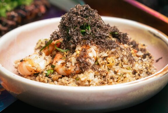 An earthenware dish with prawn fried rice, featuring a pile of grated black truffle on top as garnish.