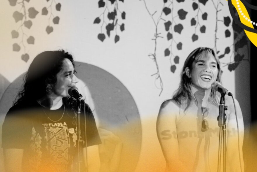 A black and white image of two women standing in front of microphones and talking, a yellow cast over the bottom of the image. 