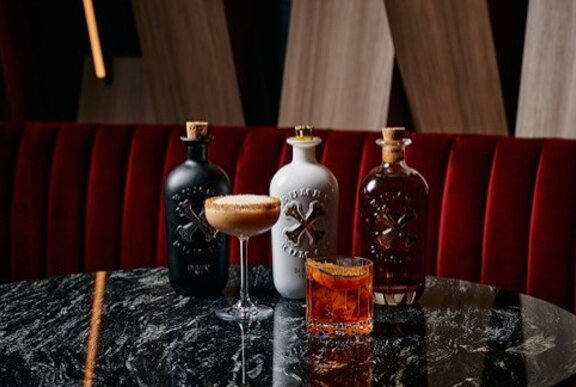 Two cocktails on a marble topped table, with three bottles of rum behind them.