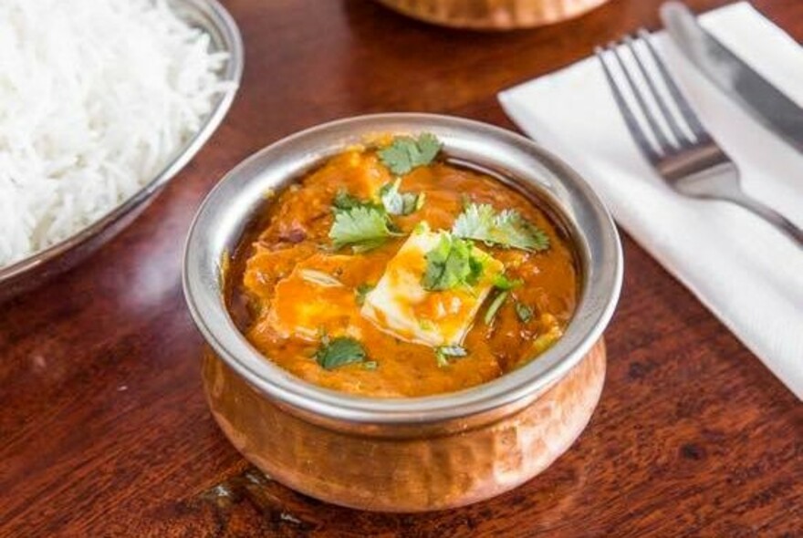 A set table with a beaten copper bowl containing curry and another bowl containing rice.