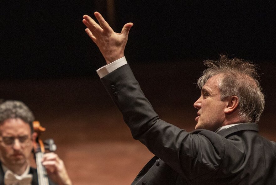 MSO Chief Conductor, Jaime Martin, with his arm in the air and a seated cellist in the background.