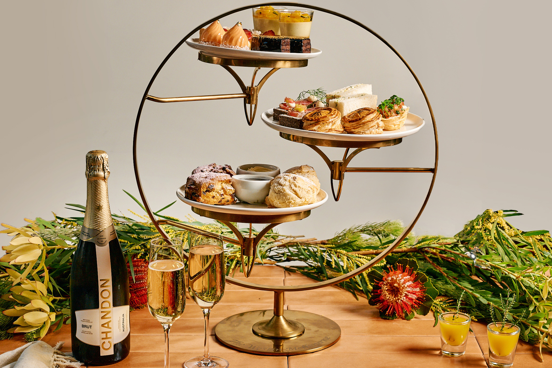 A round gold high tea stand with three plates of food, and two glasses of Chandon.