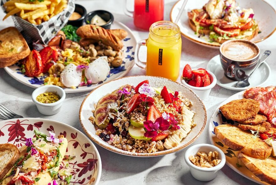 A table filled with dishes of food including breakfast plates, salads, glasses of juice and bread.