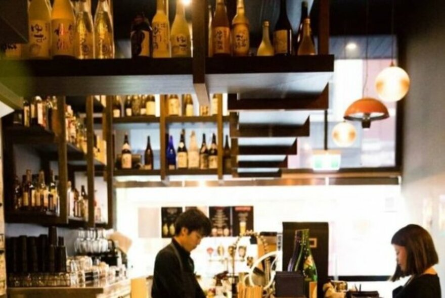 Staff in athe bar area of a Japanese restaurant with sake bottles.