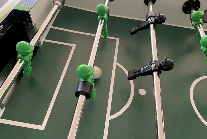 A close up of a foosball table with green and black players.