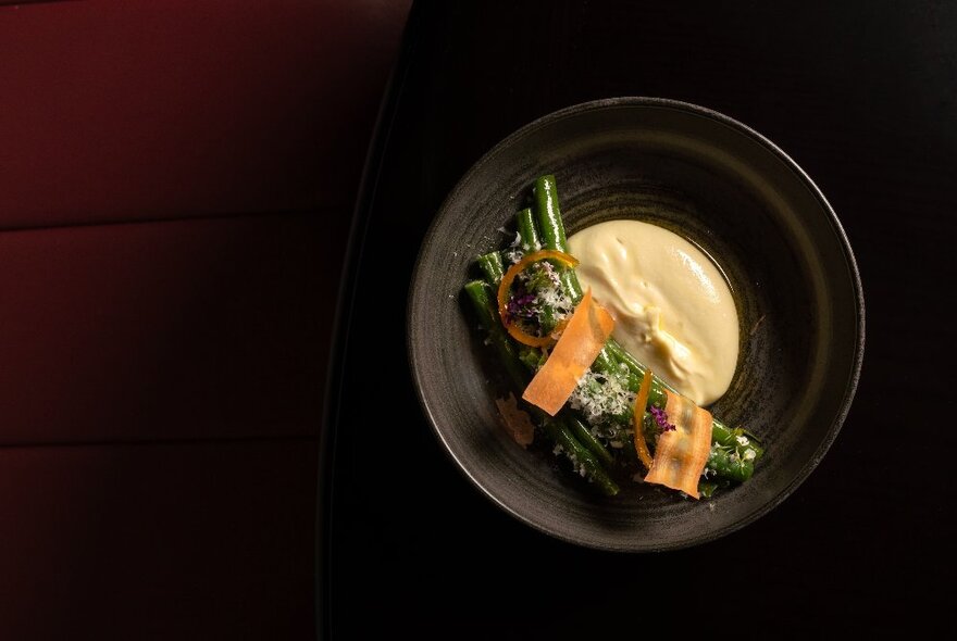 Black dish of grilled vegetables with a pool of beige sauce.