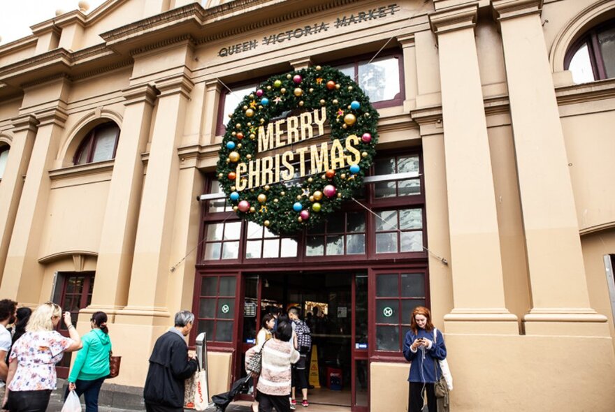 Huge Christmas wreath on the market doors at Queen Victoria Market, with marketgoers passing by.