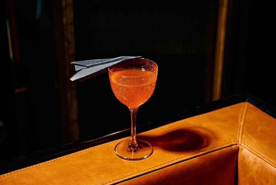 Orange cocktail with paper plane, resting on a leather chair.