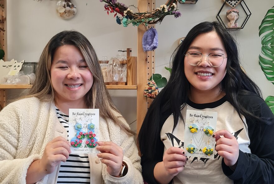 Two smiling workshop participants holding up jewellery they have made.