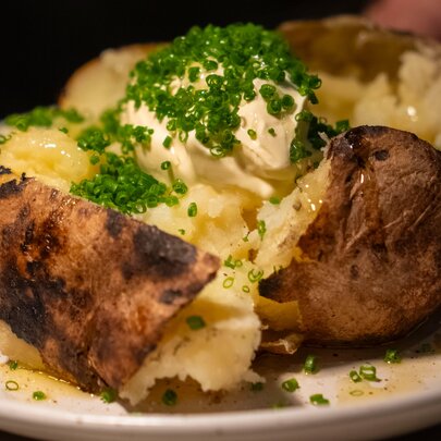 A split baked potato with sour cream, topped with chives on a white plate