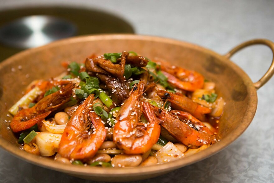 Copper dish of prawns and vegetables.