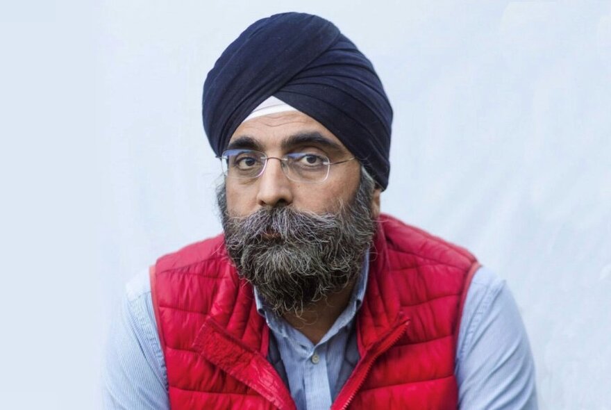 Architect and social entrepreneur, Indy Johar, wearing a red puffer vest, pale blue shirt and black turban.