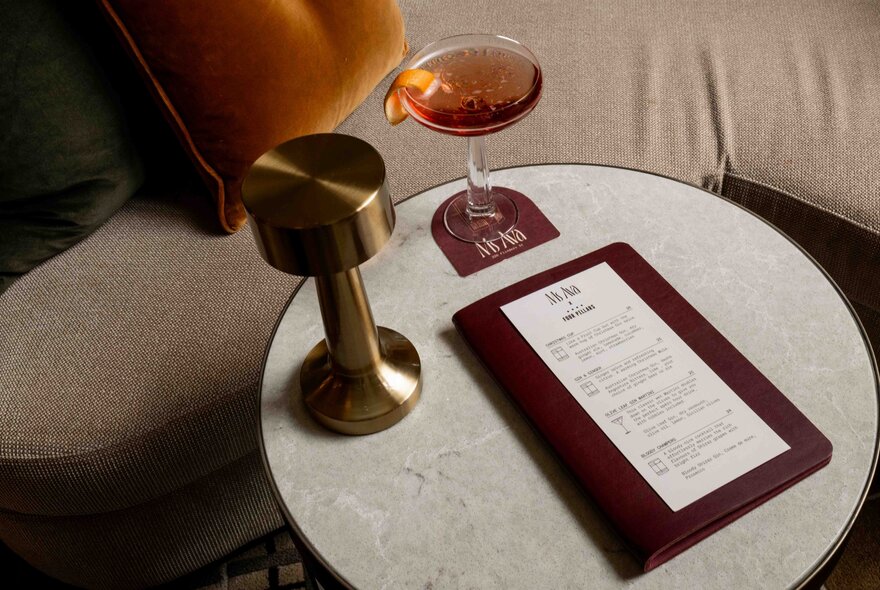 A small table with a glass of wine, a table lamo and a menu. 