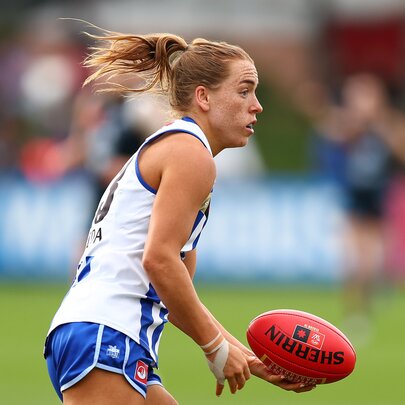 A North Melbourne AFLW player handballing a red football during a game.