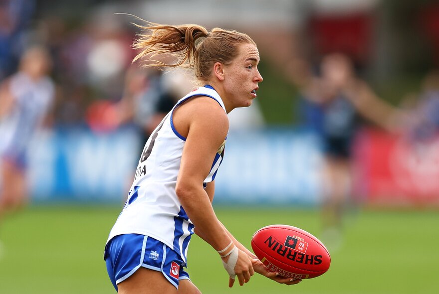 A North Melbourne AFLW player handballing a red football during a game.