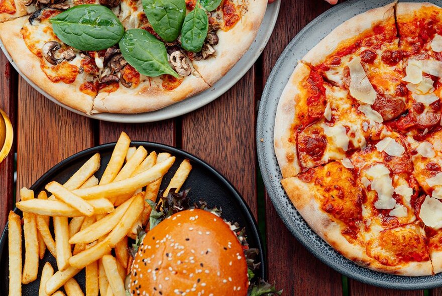 Three plates of food seen from above, including two pizzas and a burger with chips.