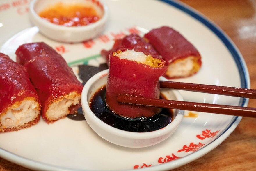 Chopsticks dipping a sliced rice roll into a thick sauce.