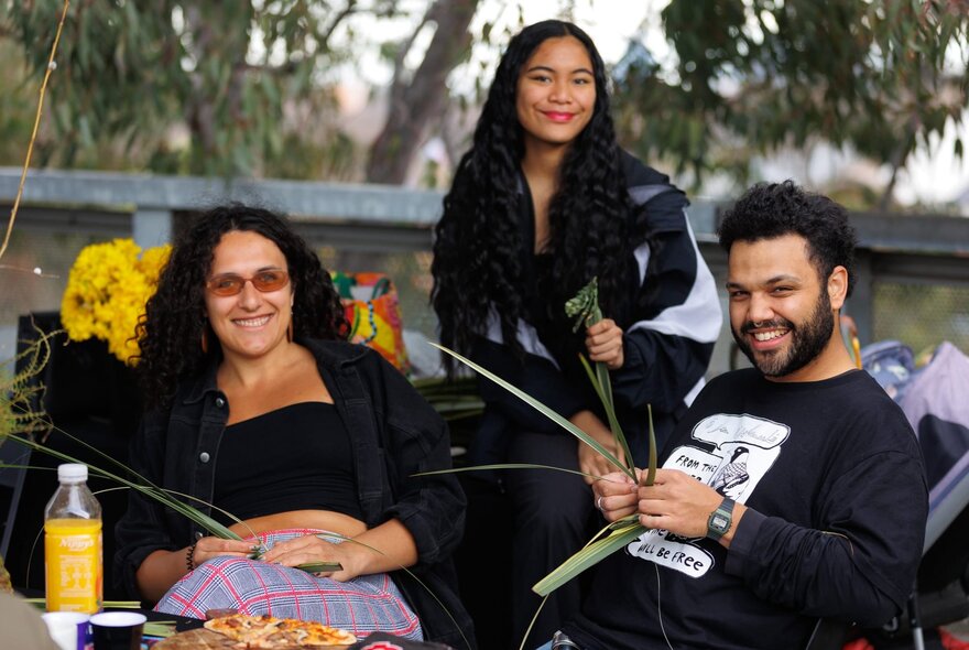 People seated with flowers and reeds in an outdoor setting with gum trees.