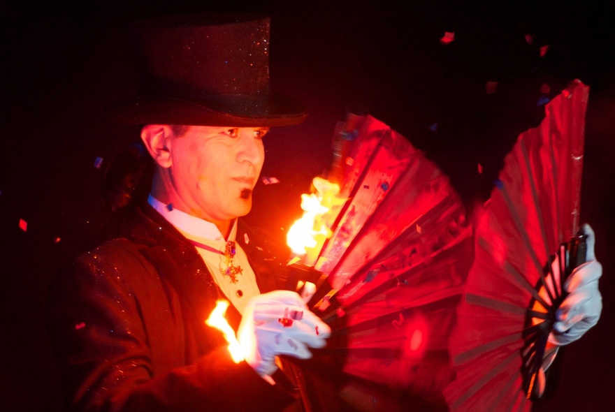 Magician wearing a top hat holding a fan with flames.