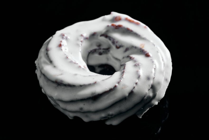 A classic vanilla-glazed choux pastry cruller, featuring a distinct twisted ring shape and glossy white icing.
