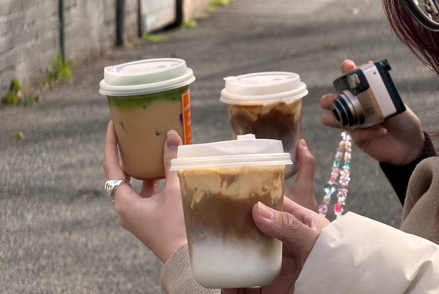 Hands holding out matcha and other iced drinks in front of a small camera. 