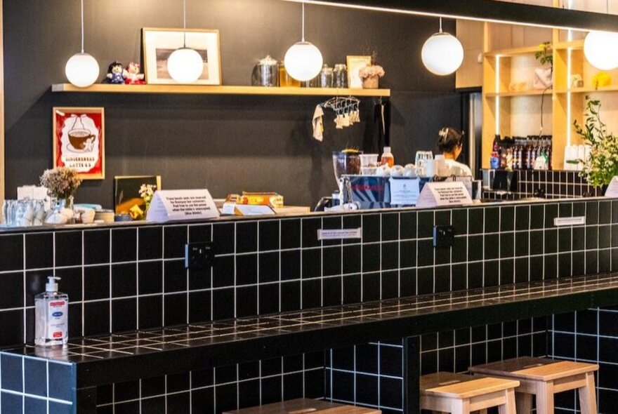 Black-tiled open kitchen area with stool seating in a cafe setting.