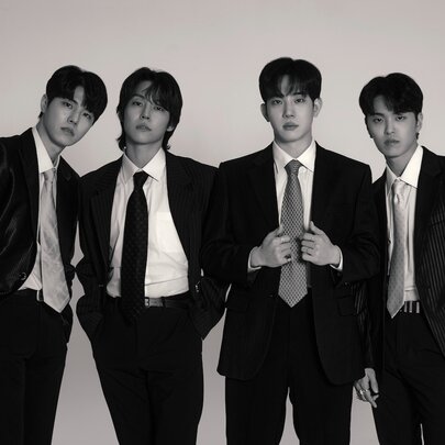 Black and white photograph of the four members of the Korean rock band, The Rose, wearing black suits and ties.